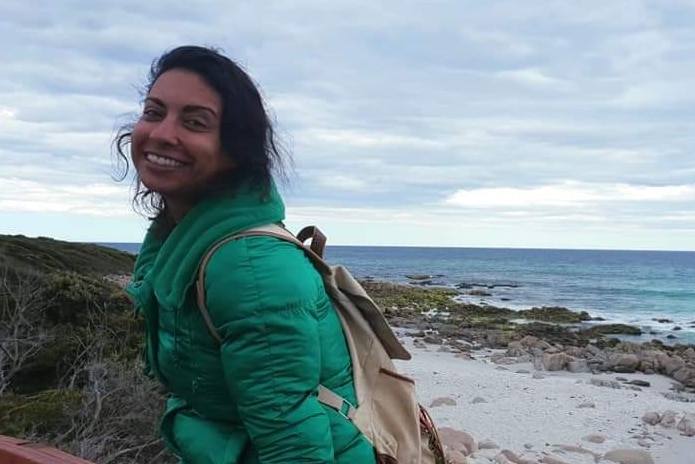 A woman wearing a green jacket sitting by the beach, smiling