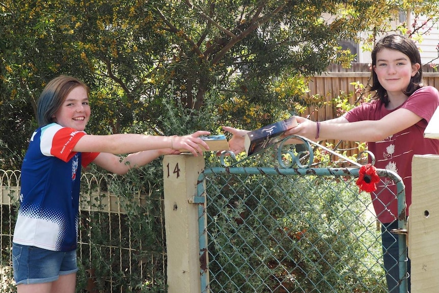 Two girls swap books over a fence