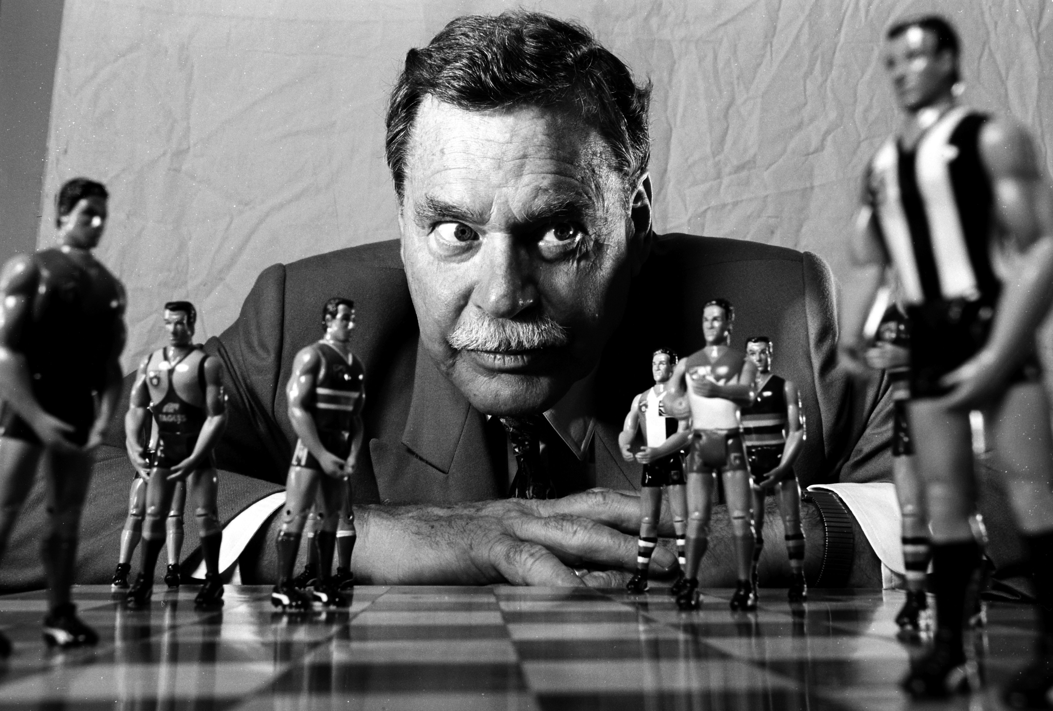 AFL legend Ron Barassi looks over a chessboard with figures of AFL players as the pieces.
