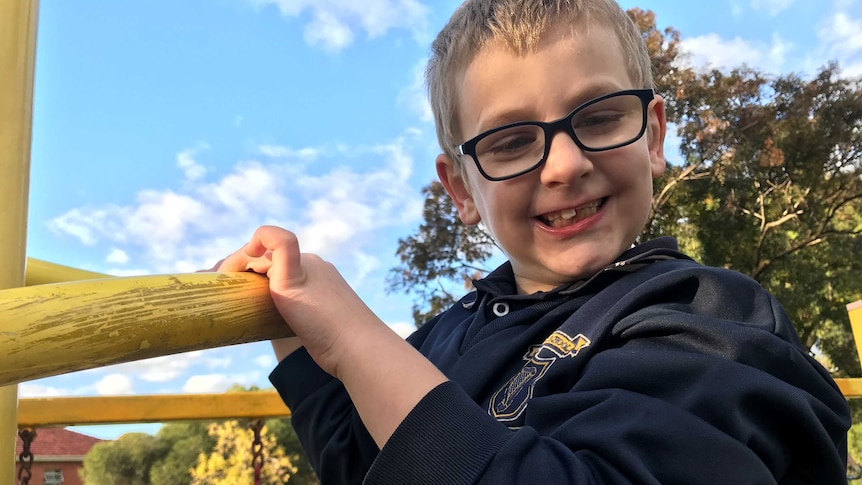 A little boy smiles at the camera while hanging off a playground.