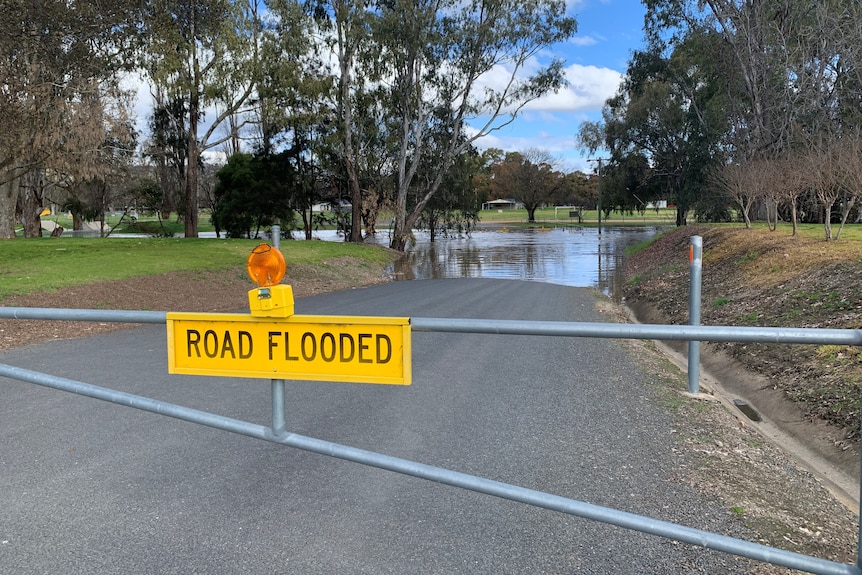 A "road flooded" sign on a gate closed in front of a flooded road