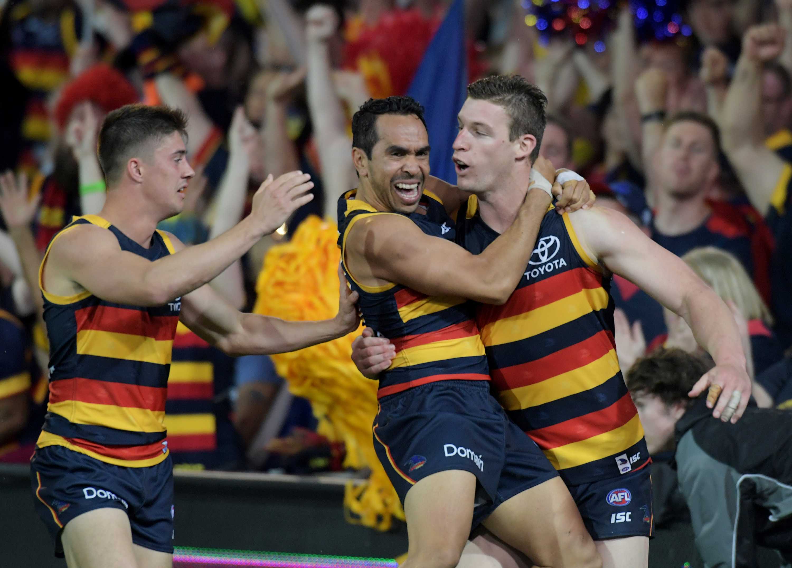 Eddie Betts jumps onto Josh Jenkins as the crowd cheers a goal in the background.