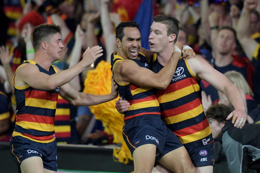 Eddie Betts jumps onto Josh Jenkins as the crowd cheers a goal in the background.