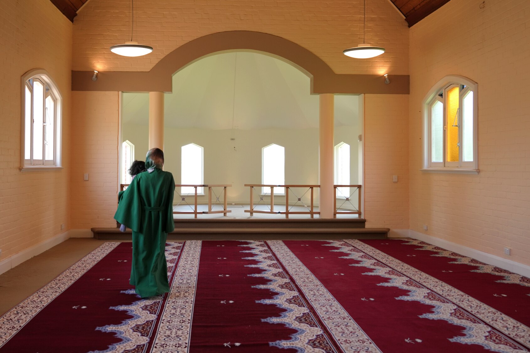 Una mujer con una abaya verde y un hiyab de seda bordado, un hombre con camisa y vaqueros y un niño de dos años caminan por la iglesia.