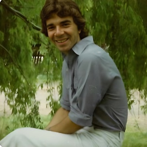 Young man smiling wearing a blue shirt looking fit sitting near a lake