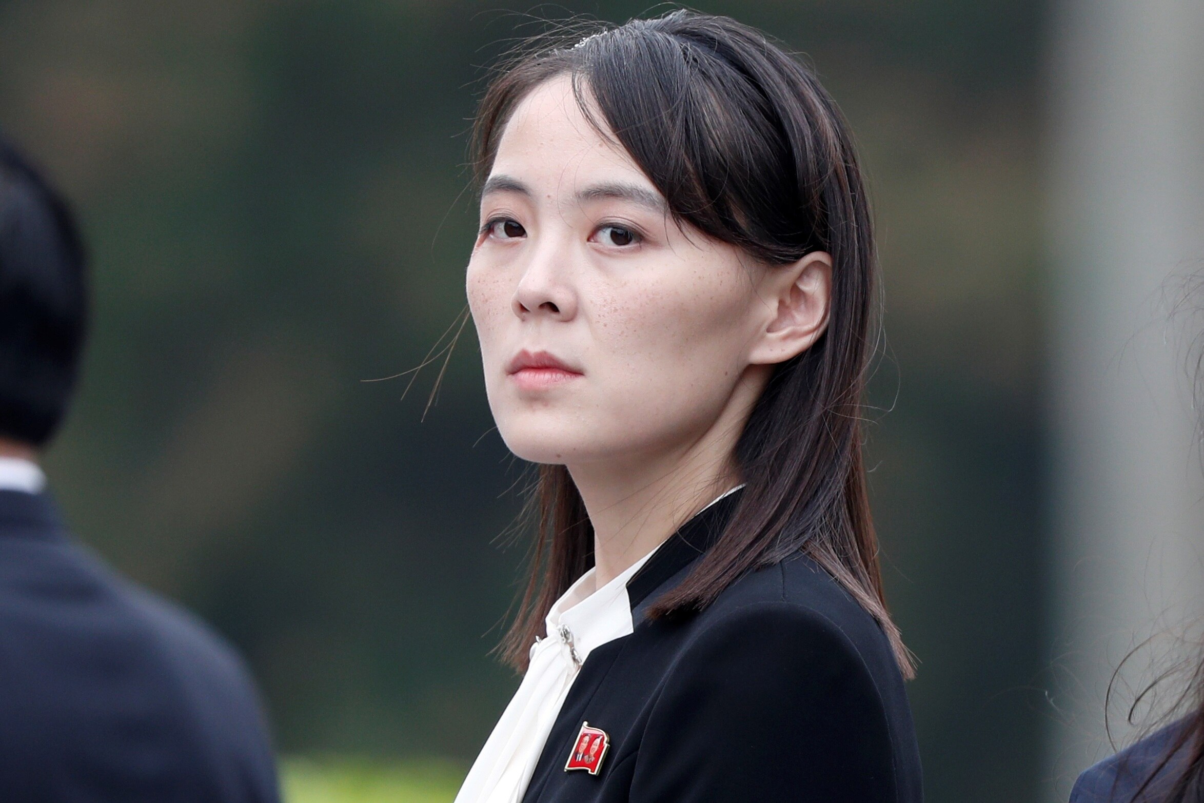 A North Korean woman in her 30s wearing a black jacket and white shirt looks directly at the camera.