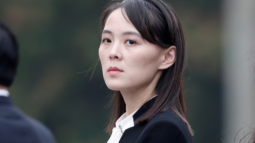 A North Korean woman in her 30s wearing a black jacket and white shirt looks directly at the camera.