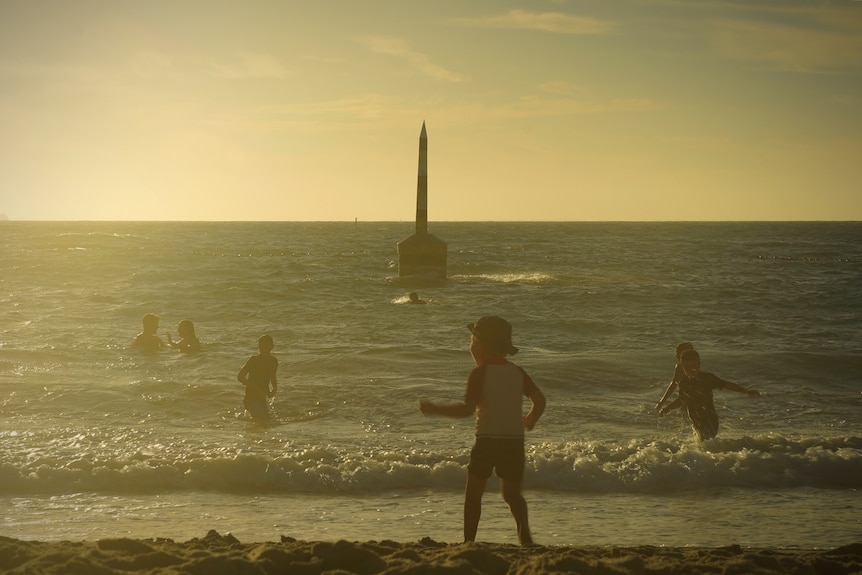 Children swim at a beach while the sun sets in the background