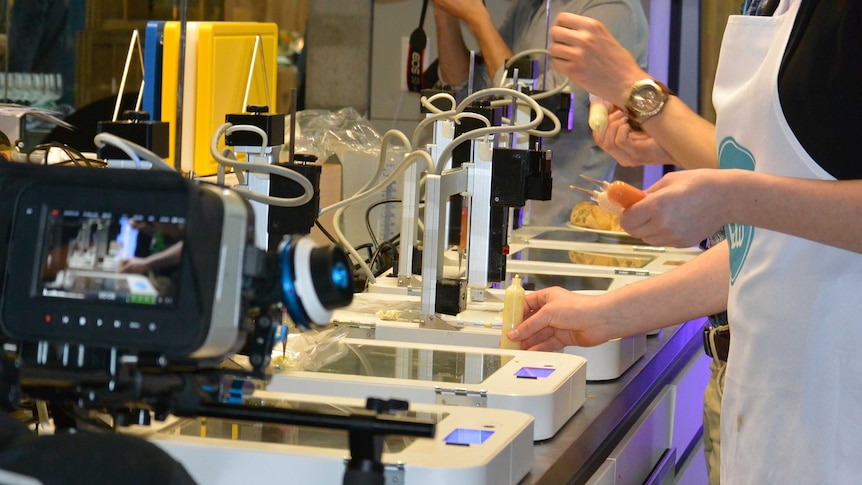 Video screen and glass topped scanners with hands holding tubes of liquid food ready for 3 dimensional printing