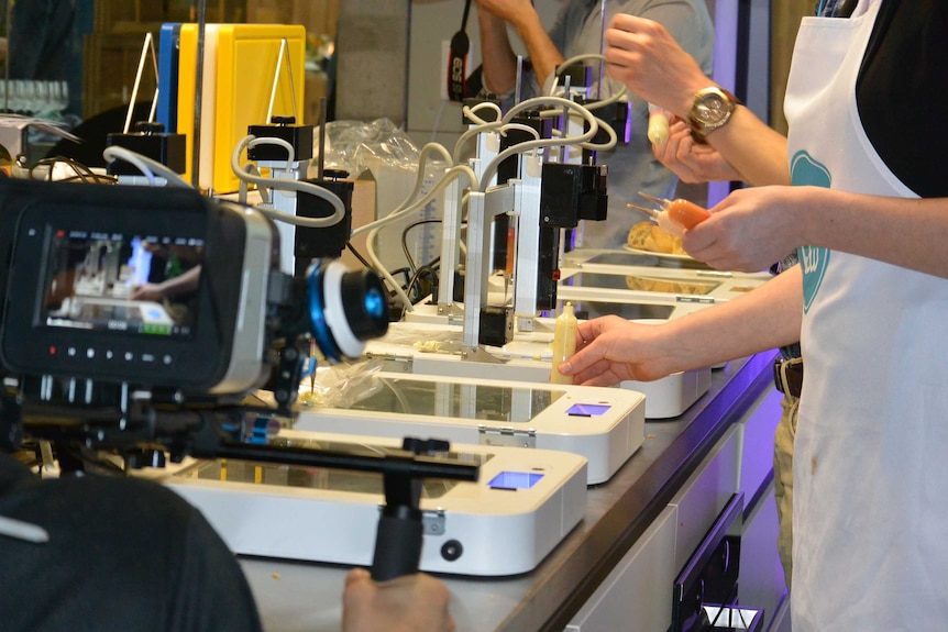 Video screen and glass topped scanners with hands holding tubes of liquid food ready for 3 dimensional printing