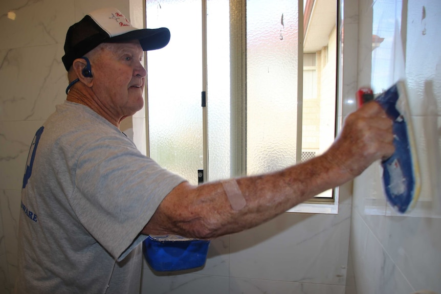 A man uses a tool in a bathroom.