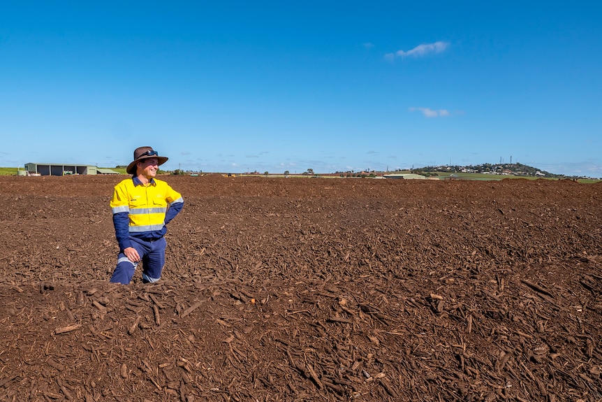 A man stands amongst large piles of compost earth.