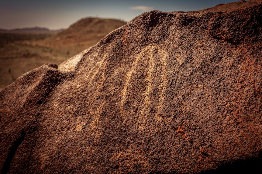 With the dusty horizon in the background, markings are seen on a rock.