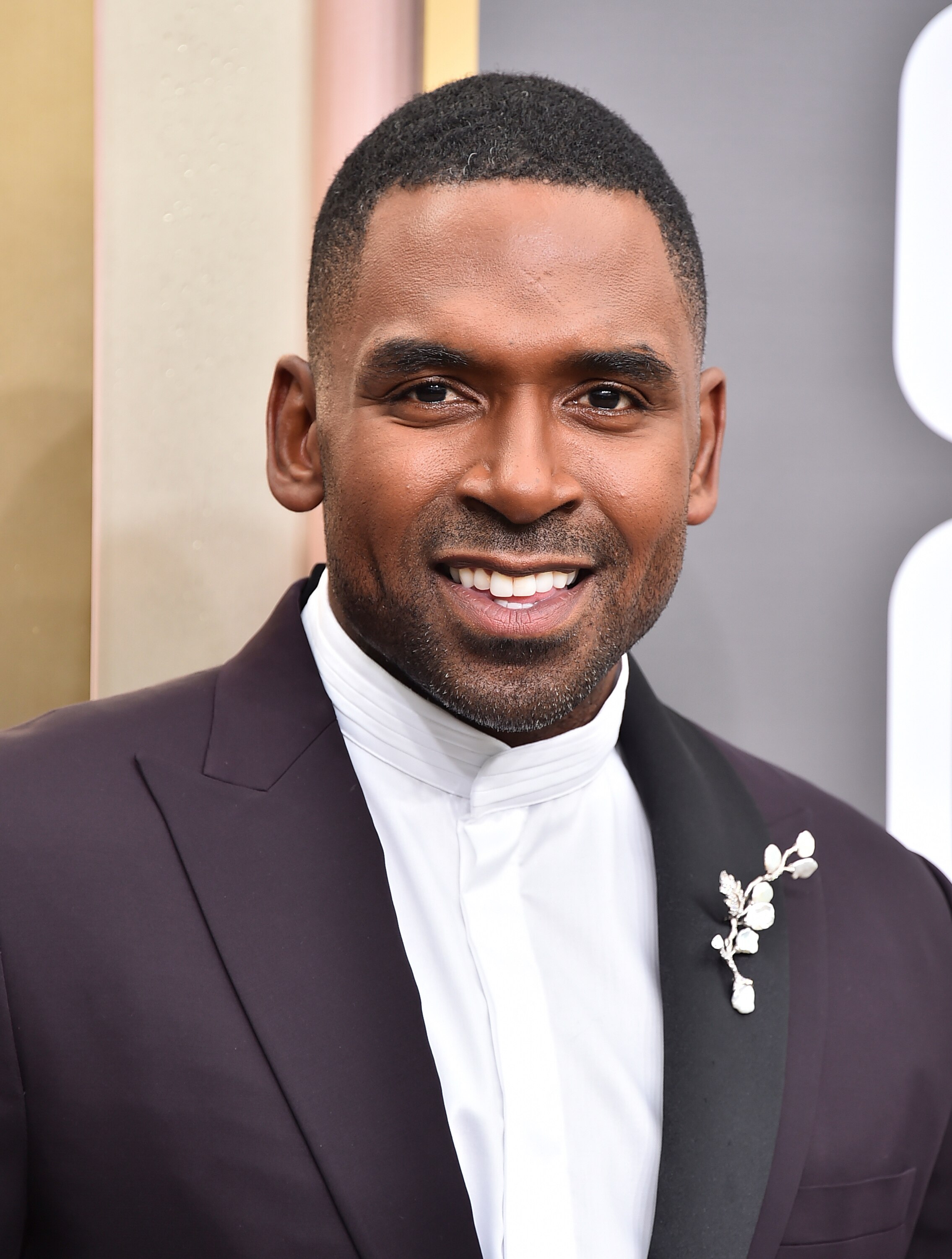 A close up of Justin Sylvester wearing a dark plum blazer with a silver, sparkly brooch that looks like a sprig of foliage. 