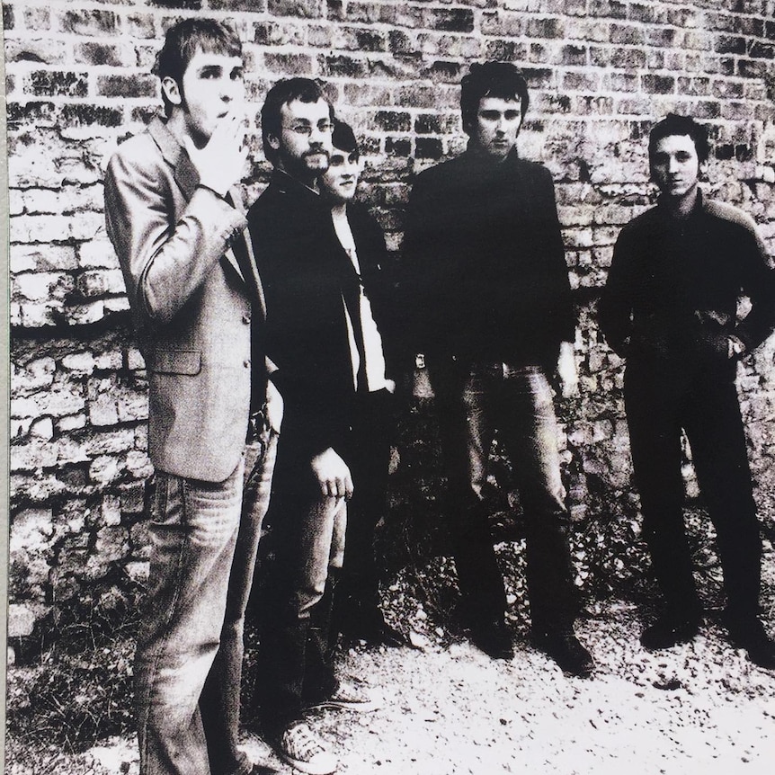 A black and white photo of The Panics standing outside a rugged brick wall
