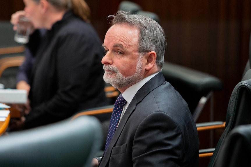 A bearded David O'Byrne sits passively at the back of Parliament.
