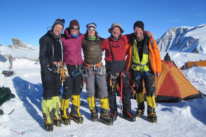 A group of five mountaineers with ropes and crampons high in snowy mountains