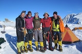 A group of five mountaineers with ropes and crampons high in snowy mountains