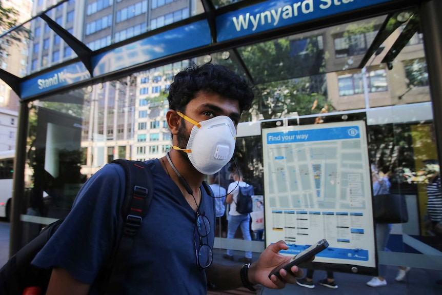 A man wears a face mask as he waits for a bus in Sydney.