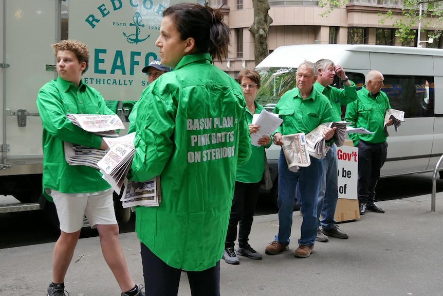 A group of people with green shirts stand on a Melbourne street handing out flyers