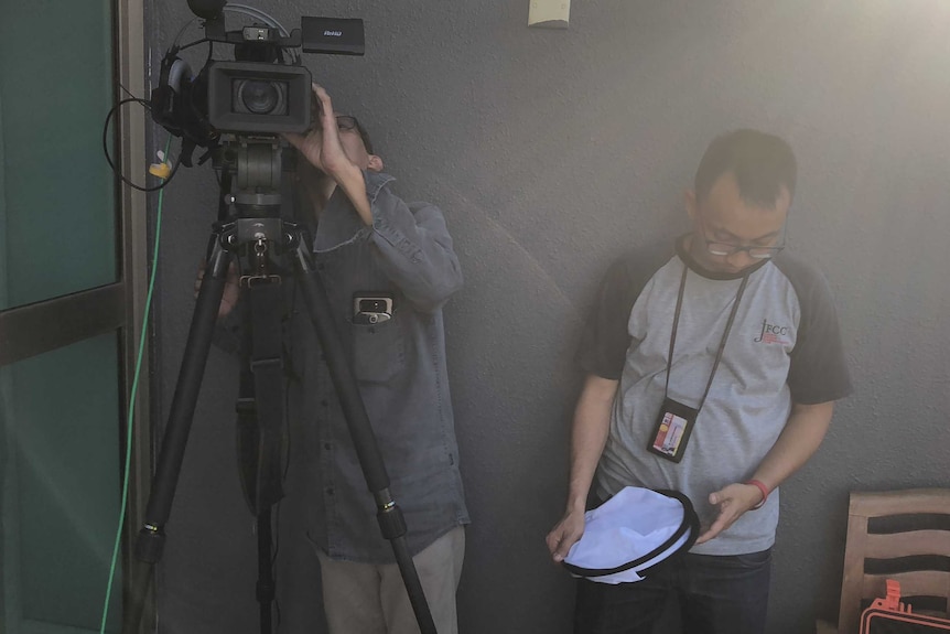 Cameraman looking in viewfinder and producer looking at diffuser while standing on hotel balcony.