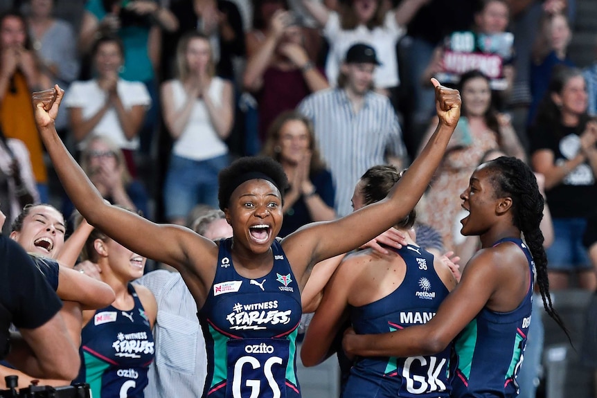 A smiling netballer raises her arms wide in celebration after the Super Netball grand final.
