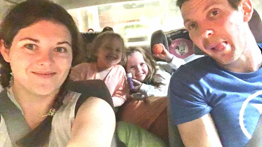 A man and woman in a car with two young girls in the back seats all looking at the camera.