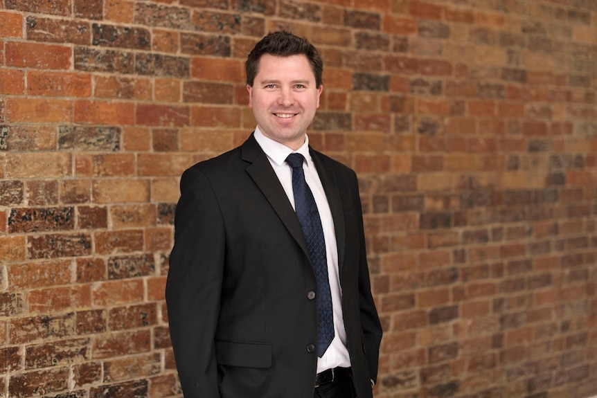 Lawyer Joshua Brown smiles as he stands in front of a brick wall in Brisbane.