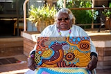 An Aboriginal woman holds a painting.