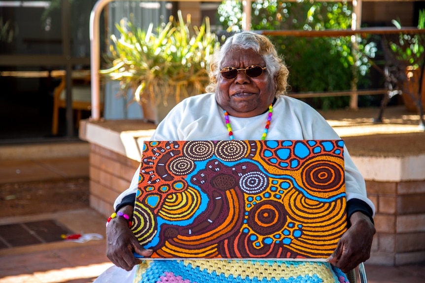 An Aboriginal woman holds a painting.