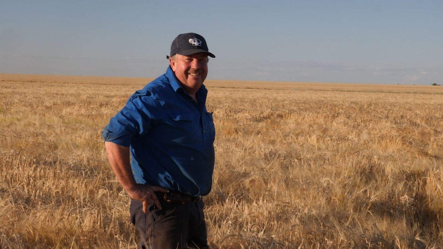 A smiling farmers stands in a field of barley