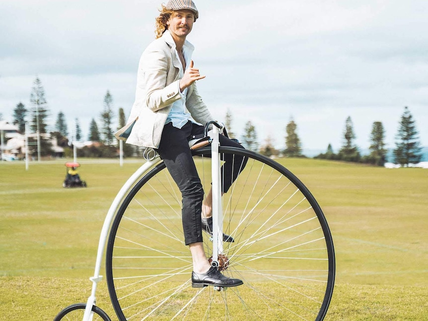 A young man riding a penny-farthing bicycle