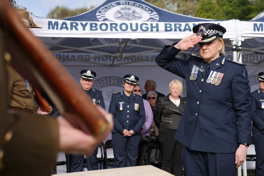 A female police officer, medalled of breast and sombre of countenance, salutes at a memorial event.