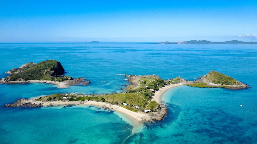 aerial shot of green boot-shaped island surrounded by blue water and coral reef with white beaches and beachfront cottages.