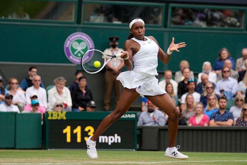 A female tennis player is at full extension in the act of hitting a forehand at Wimbledon.