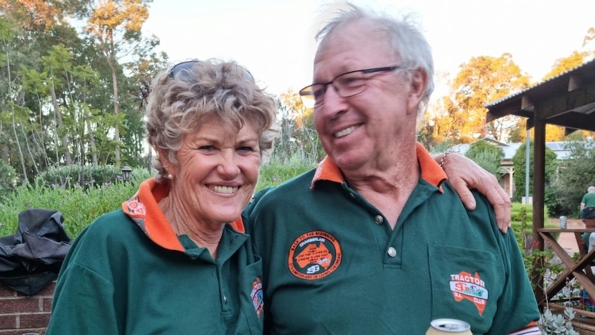 A woman and a man aged in their 60s stand smiling arm in arm wearing matching green polo shirts
