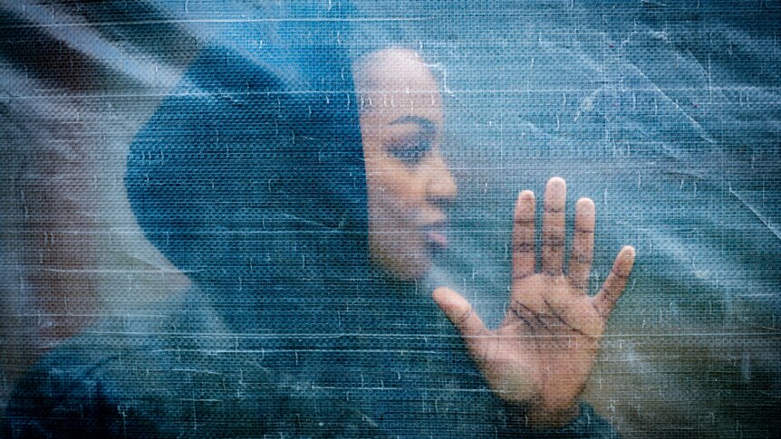 A young woman of African descent is seen through a plastic sheet with her hand pressed up against it