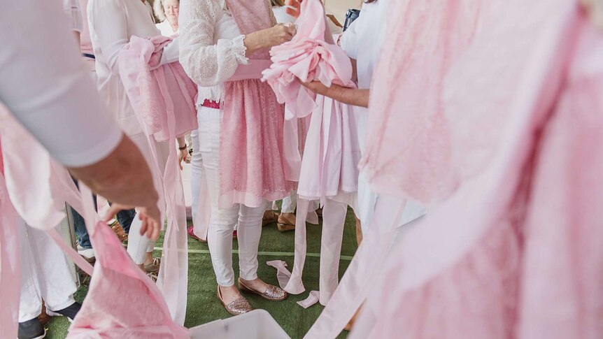 A close up of a woman handing out pink aprons to a group of women.