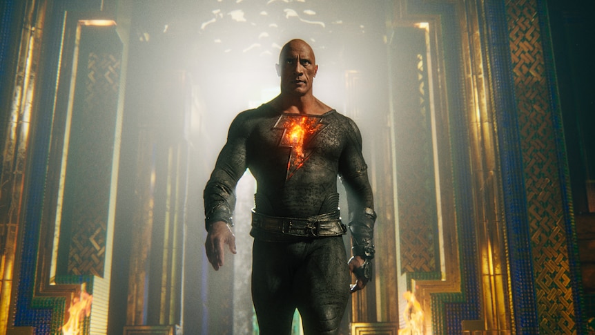A bald Black man wearing armour, including a fire-branded undershirt, strides purposefully through an ornate room
