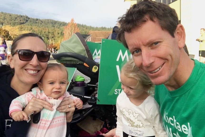 Michael Wait smiles in a green campaign shirt with wife Whitney and their two daughters at the time.