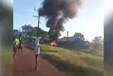 A house burns as people stand around.