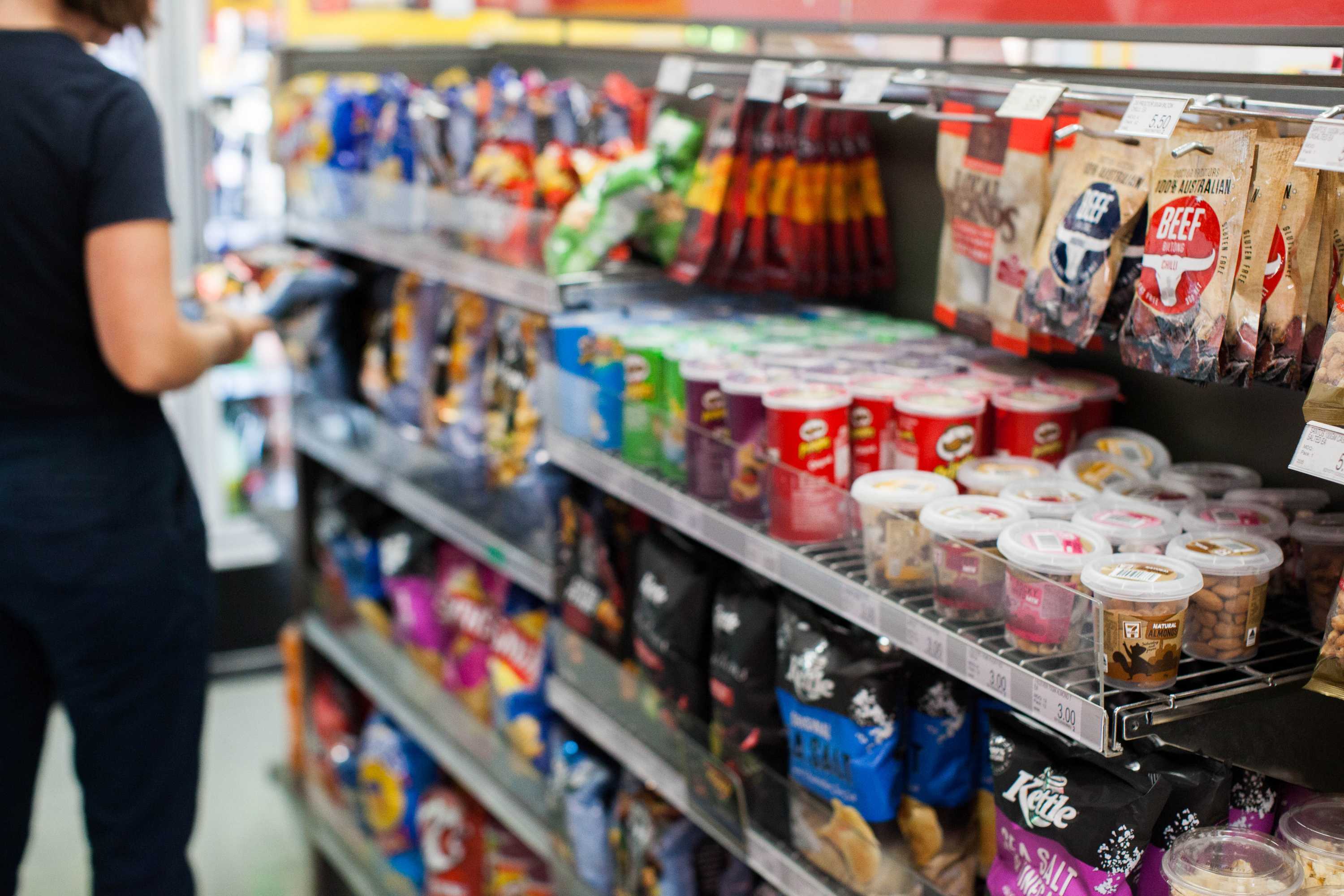 A person looks at a packet of chips in a supermarket or convenience store.