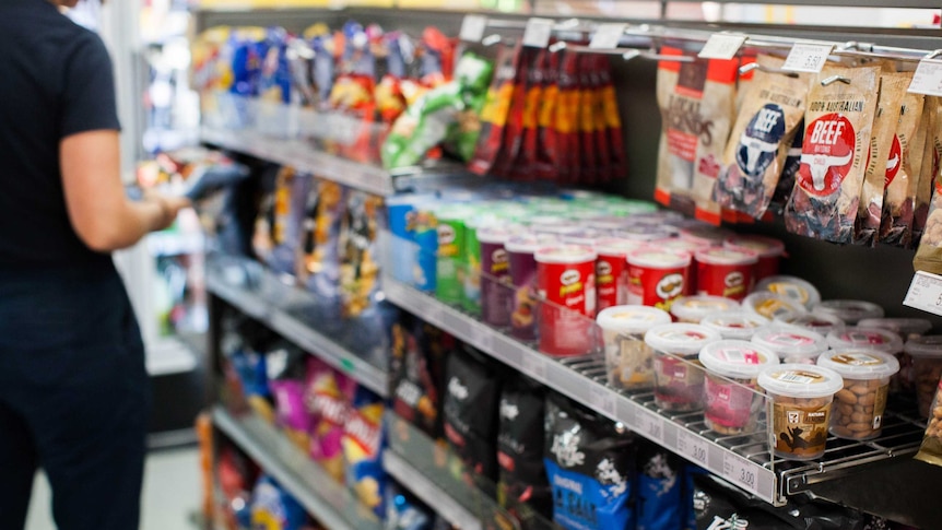 A person looks at a packet of chips in a supermarket or convenience store.