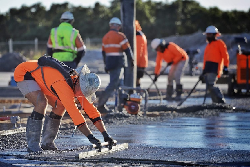 Рабочий разглаживает бетон во время заливки плит на фоне других рабочих.