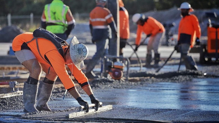 worker smooths concrete at a slab pour with other workers in background.