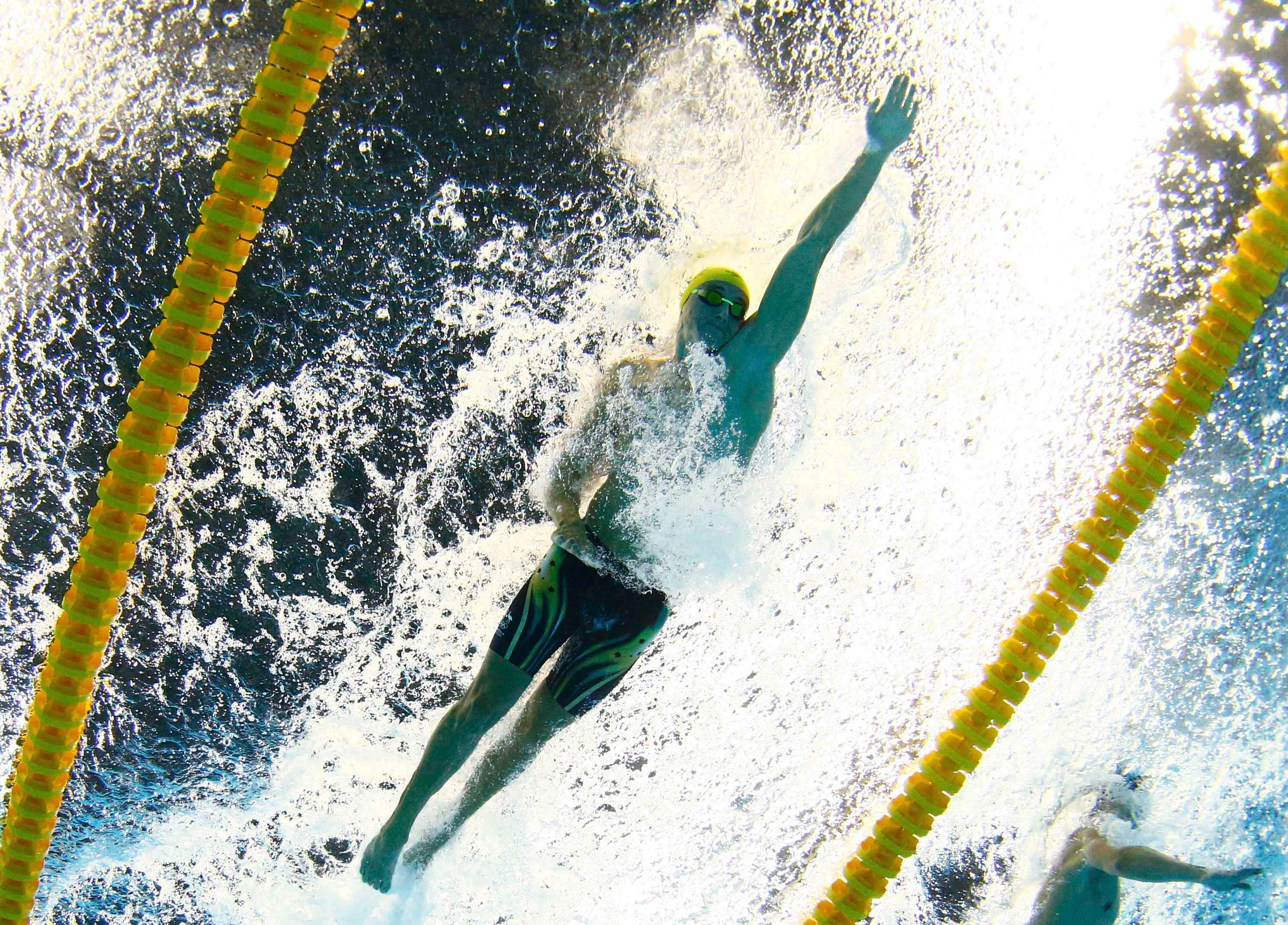 Swimmer, goggles, cap, underwater, swims inside yellow lane markers, water frothy around him.