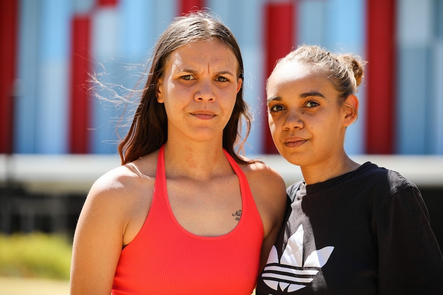 Deux femmes se tiennent debout pour une photo à l'extérieur avec des regards sérieux sur leurs visages.