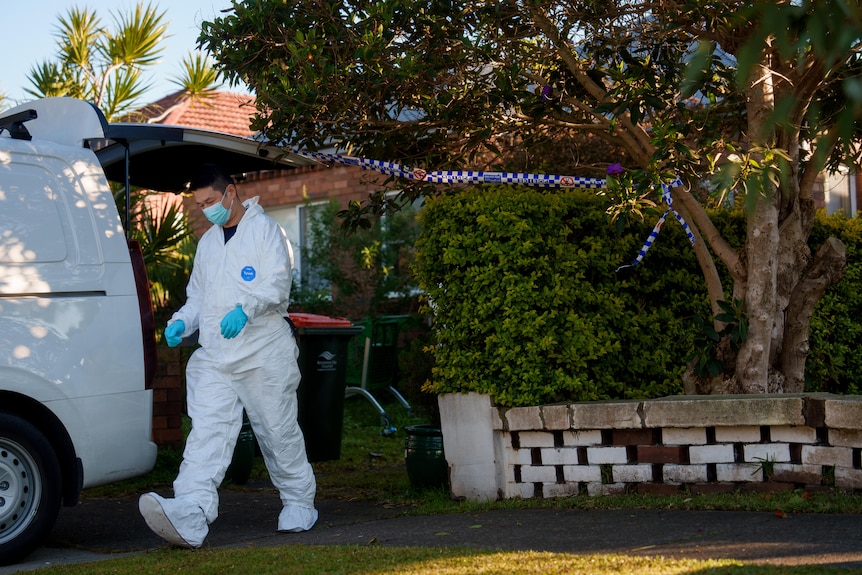 Policeman in white hazmat suit walking outside a home to a white van