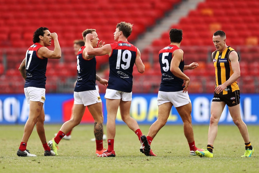 A group of AFL footballers crowd around a goalscorer in celebration.