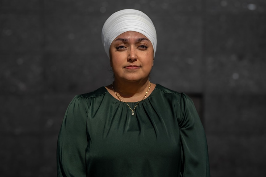 Guntaak Laur, dessed in a dark top and a white turban, is pictured against a black background. She looks directly at the camera.
